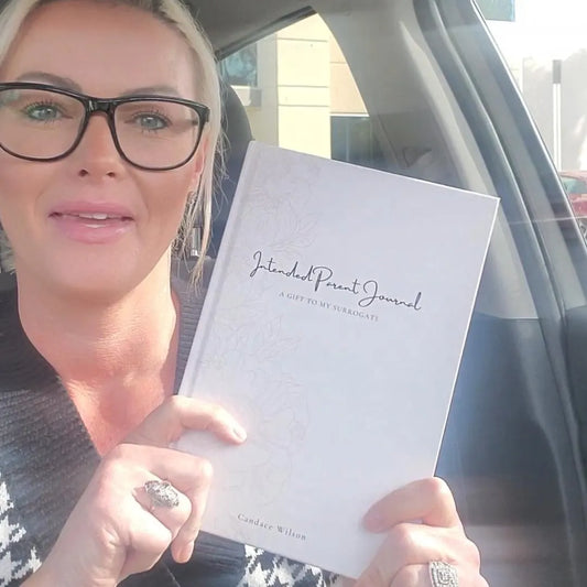 Woman holding a book titled 'Intended Parent Journal' inside a vehicle.